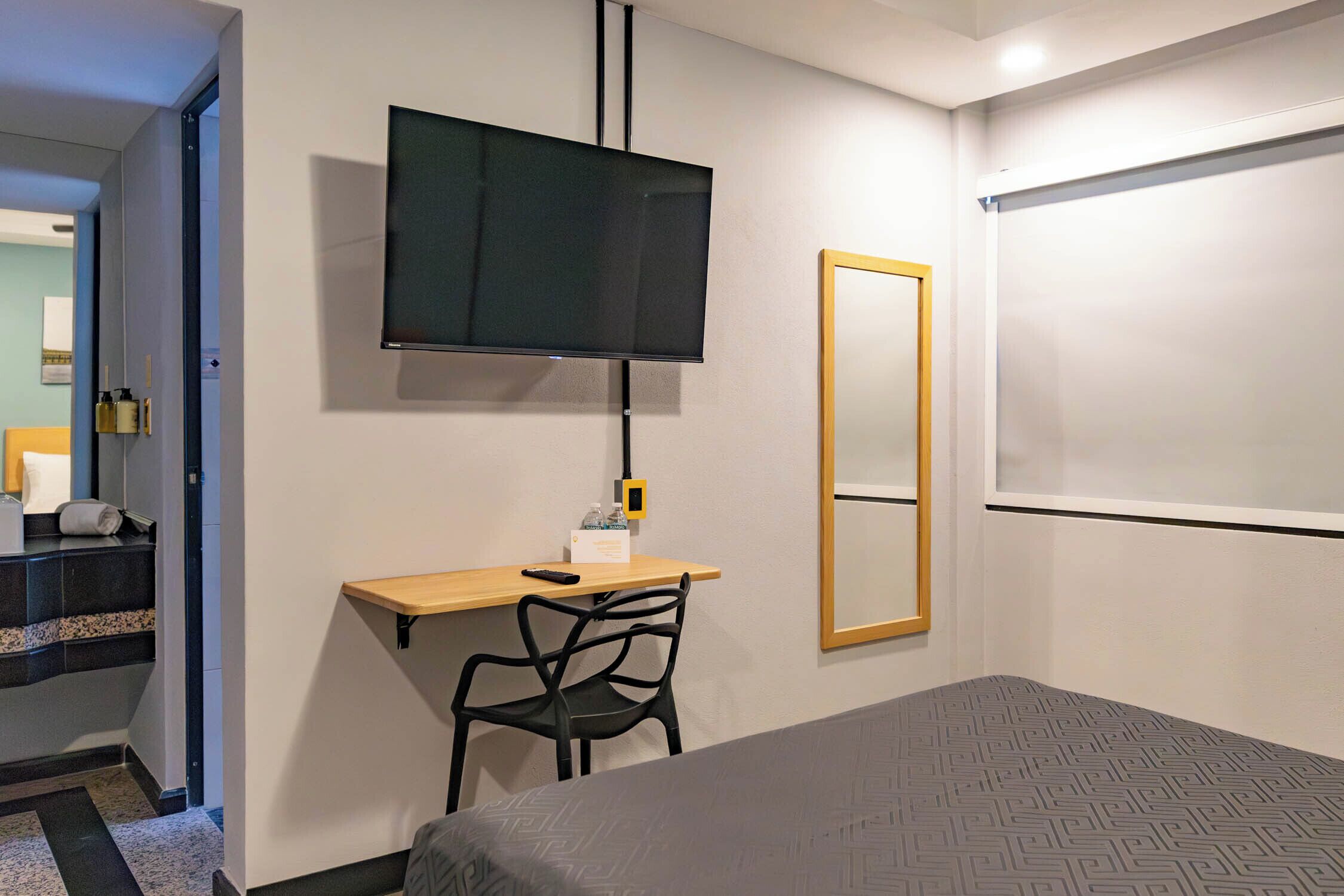 A hotel room with a bed, a desk with a chair, a television, a mirror, and a door leading to a staircase.