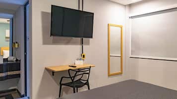 A hotel room with a bed, a desk with a chair, a television, a mirror, and a door leading to a staircase.