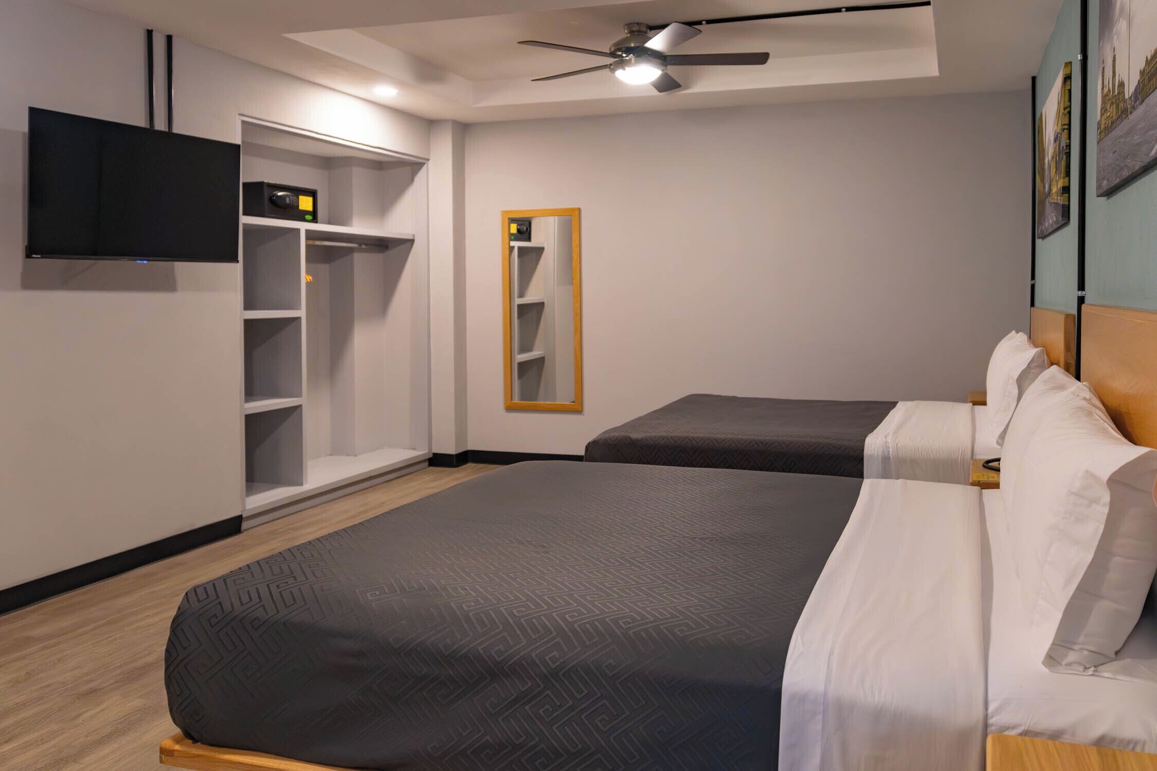 Ein Hotelzimmer mit Bett, Kleiderschrank, Fernseher und Deckenventilator.