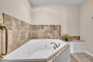 Un baño con una bañera grande, un pasamanos y una planta en maceta.