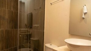 Et badeværelse med en glasvæg omkring brusebad, toilet og et spejl over vasken.