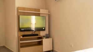Et moderne værelse med et indbygget TV på et træstel, en lille hylde med en plante og en hvid seng.