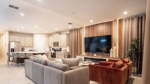 A modern living room with a grey sectional sofa, a red velvet sofa, and a flat-screen TV mounted on a wooden wall. - 8BR Home with Pool & Theater at Solara Resort (Kissimmee)