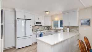 A modern kitchen with white cabinetry, a central island, a microwave, a stove, and a sink. - Island Beach Club 240F | Exquisite Oceanfront Residence | Sun, Sea and Sand (Sanibel)