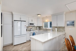 A modern kitchen with white cabinetry, a central island, a microwave, a stove, and a sink. - Gorgeous Oceanfront Condo at 240F Island Beach Club (Sanibel)