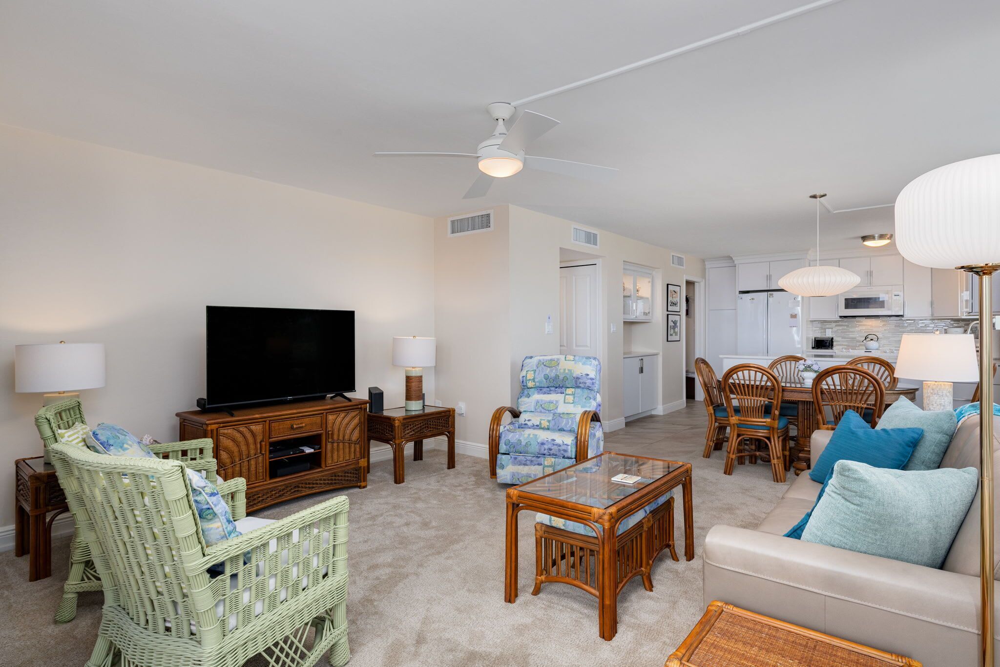 A living room with a television, wicker furniture, a glass coffee table, and a ceiling fan.