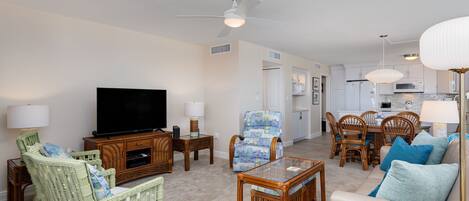 A living room with a television, wicker furniture, a glass coffee table, and a ceiling fan.
