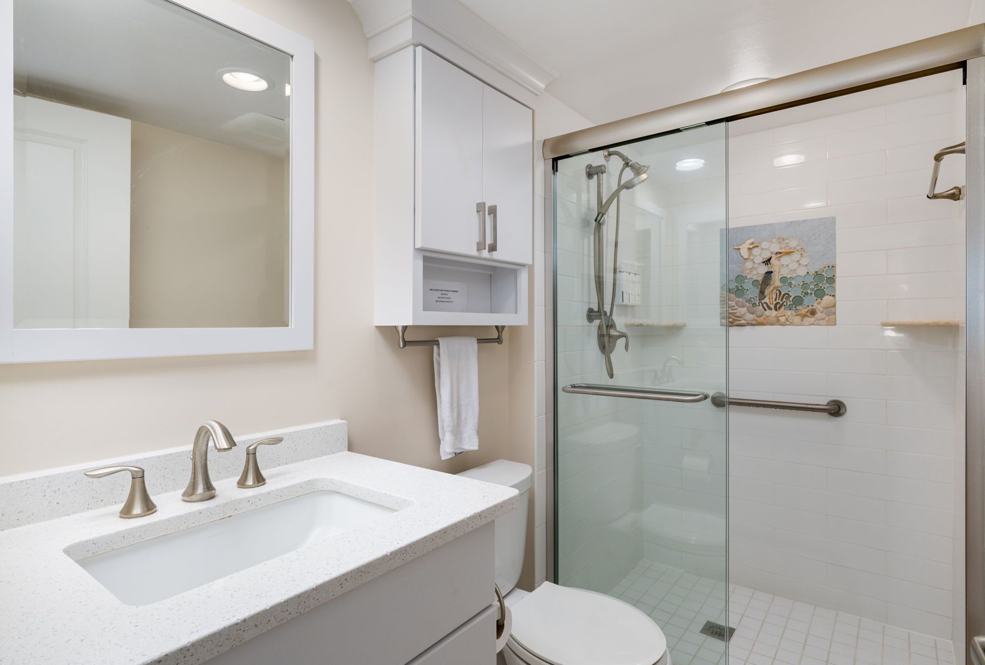 Een badkamer met een wit wastafel, drie kranen, een toilet en een douche met glazen wanden en een handgreep.