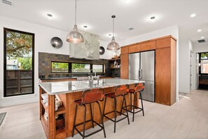 A modern kitchen with a large island, bar stools, stainless steel appliances, and pendant lighting. - Secluded Luxury Home with Pool - The Marsian! (Austin)