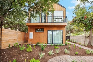 A modern two-story house with a wooden exterior, a balcony with outdoor furniture, and a garden with various plants. - Secluded Luxury Home with Pool - The Marsian! (Austin)