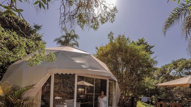 A covered outdoor area with a hot tub, wooden deck, and a glass enclosure with a person inside.