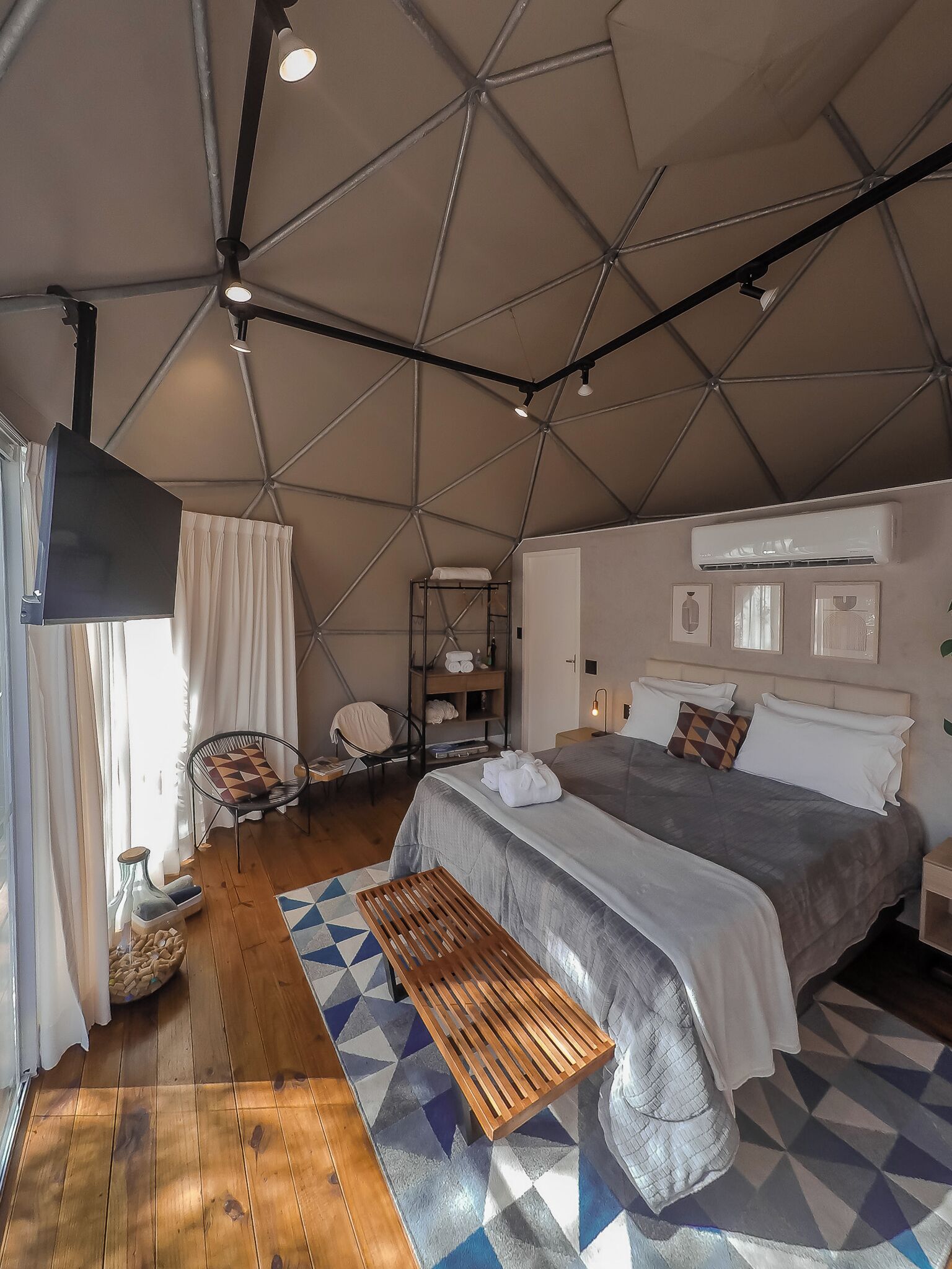 A spacious bedroom with a large bed, a wooden bench, a chair, and a shelf with towels.