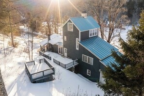 Une maison à deux étages avec un toit bleu, entourée d’un paysage enneigé et d’arbres.