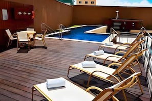 Een terras met ligbedden, een zwembad en een kleine tafel met stoelen.