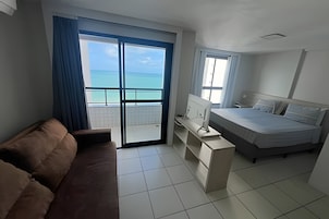 Quarto de hotel com cama, escrivaninha, sofá e vista para o oceano.