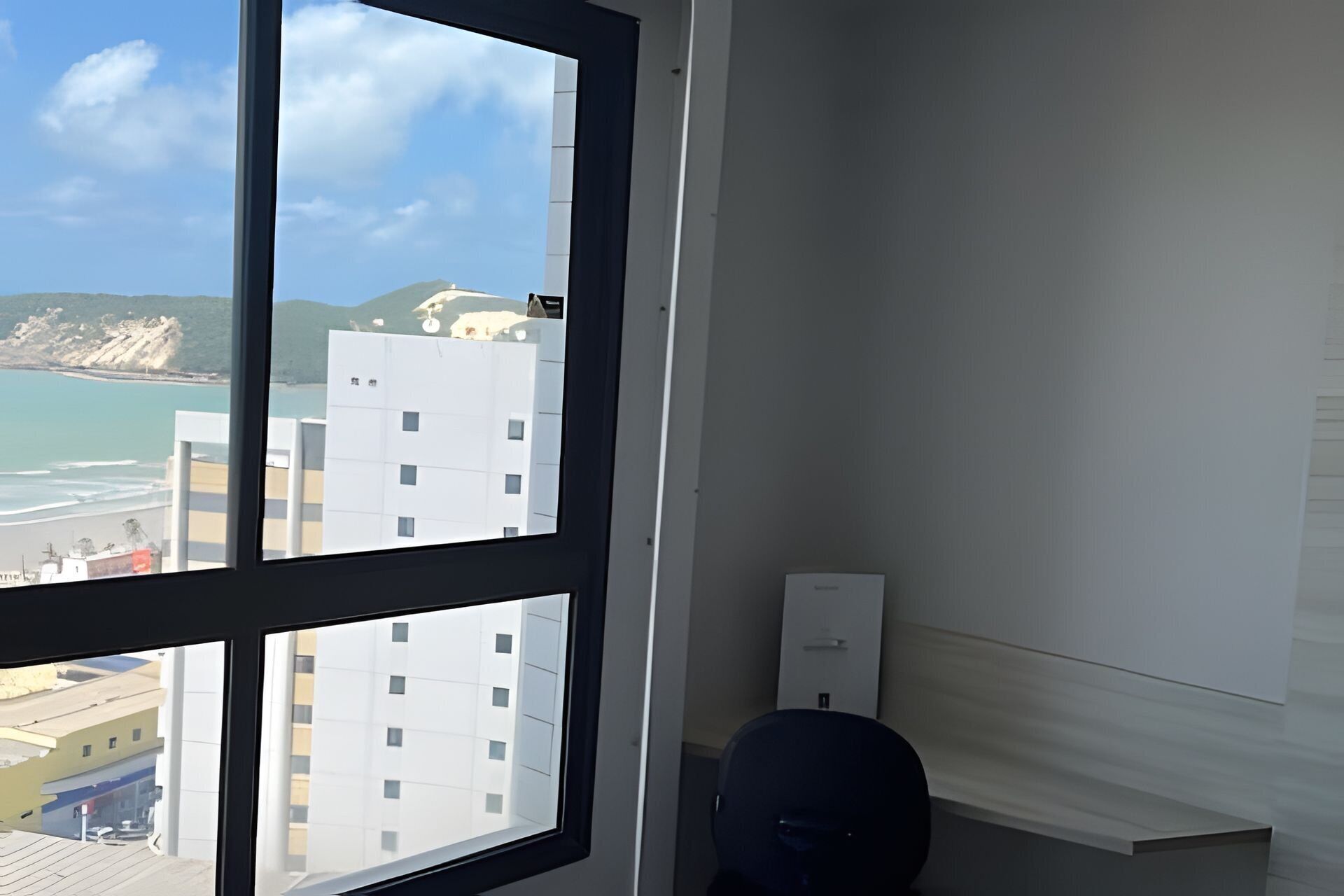 A room with a large window overlooking a beach and buildings, a white wall, and a door.