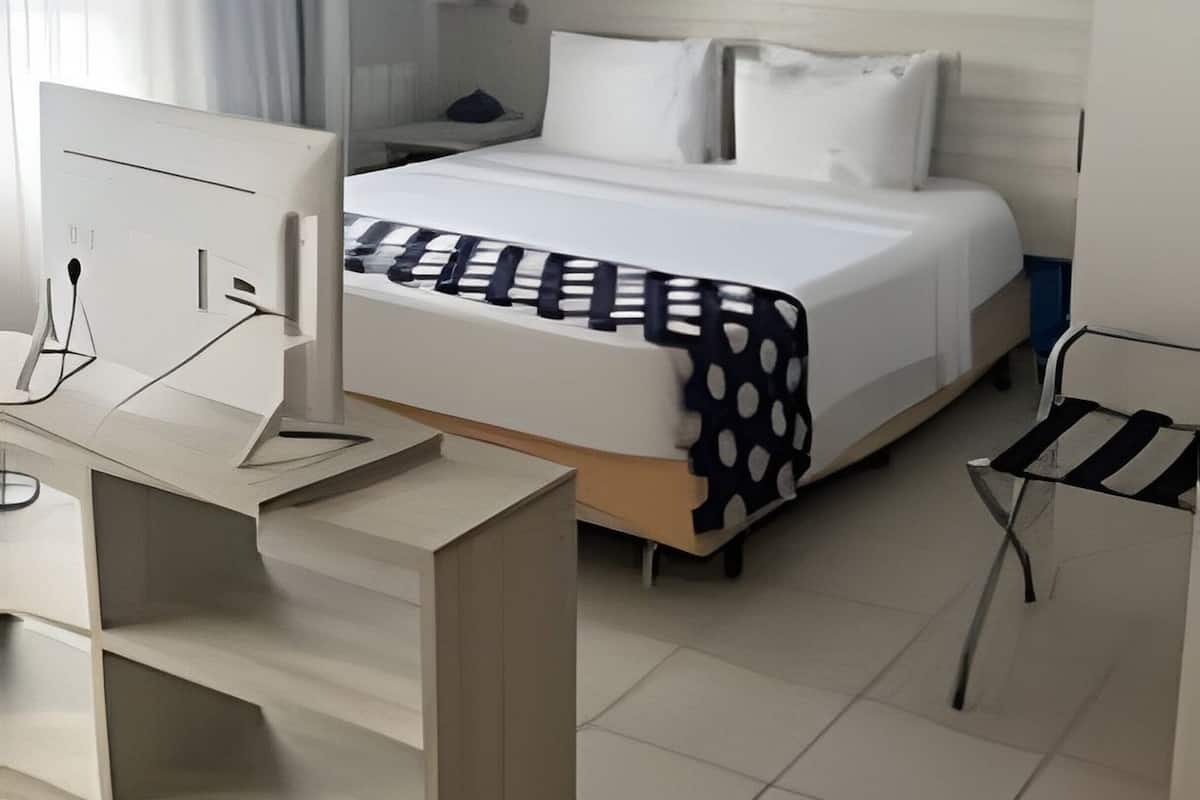 Een hotelkamer met een bed, een bureau, een stoel, een televisie en een raam met gordijnen.