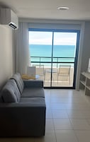 Quarto moderno com um sofá cinzento, uma pequena mesa e vista para o oceano através de grandes portas deslizantes.