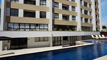 Un hotel de varios pisos con piscina, balcones con plantas y cielo despejado.