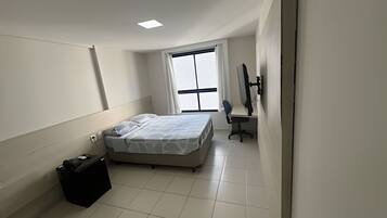 Um quarto com uma cama, uma escrivaninha, uma cadeira, um computador e uma janela.