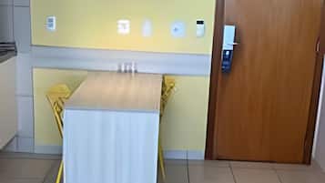 A room with a tiled floor, a wooden door, a white table with yellow chairs, a yellow pendant light, and a small painting on the wall.