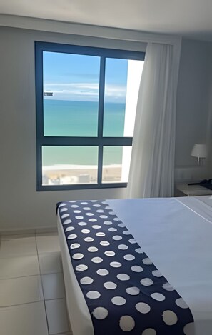 A hotel room with a bed, a window with a view of the sea, and a nightstand with a lamp. - Mar e Descanso  (Natal)