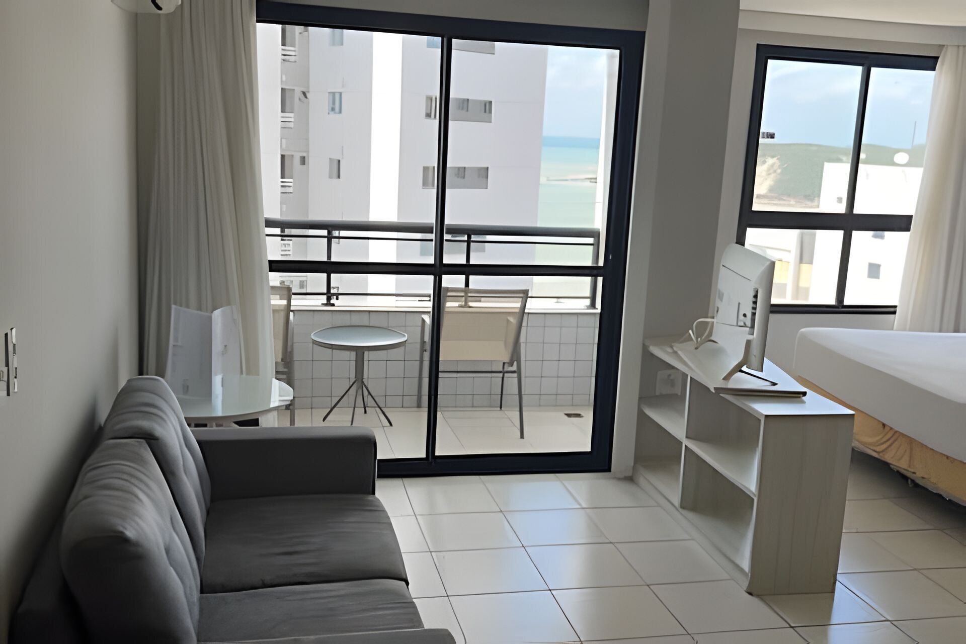 Una habitación de hotel con balcón, escritorio con computadora, sofá y cama.