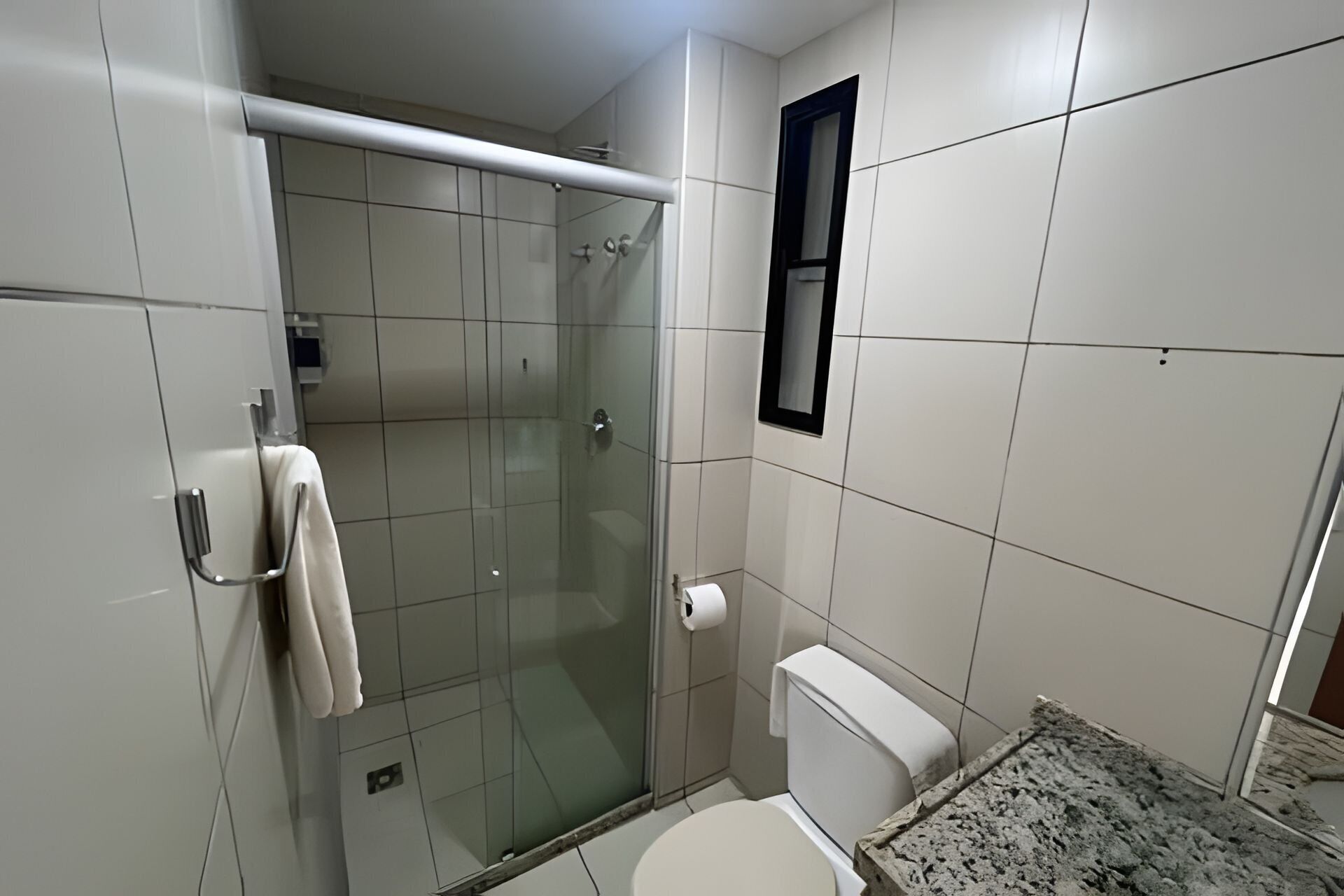 Uma casa de banho pequena e moderna com cabine de duche em vidro, sanita e suporte para toalhas.