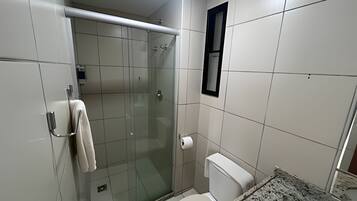 Uma casa de banho pequena e moderna com cabine de duche em vidro, sanita e suporte para toalhas.