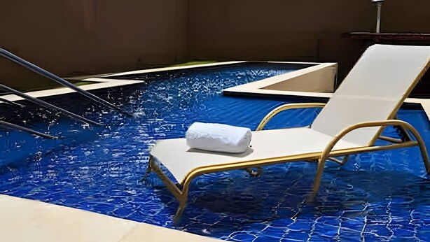 Une piscine avec un seul fauteuil de relaxation et une serviette, le tout entouré d’un mur brun.