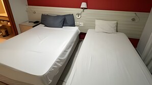 Une chambre d’hôtel avec deux lits, un mur d’accent rouge, une table de chevet avec une lampe et un tableau.