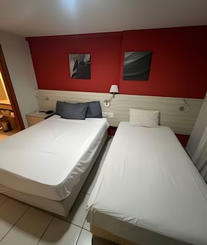 A hotel room with two beds, a red accent wall, a nightstand with a lamp, and a painting. - Mar e Descanso (Natal)