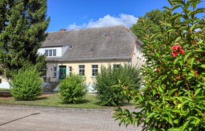A two-story house with a tiled roof, a front porch, and a well-maintained garden with various shrubs and a flowering plant. - Beautiful home in Kletzin with sauna (Kletzin)