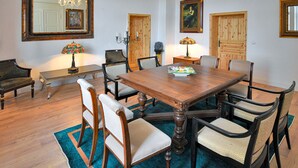 Uma sala de jantar com uma mesa de madeira, seis cadeiras, um lustre e obras de arte nas paredes.