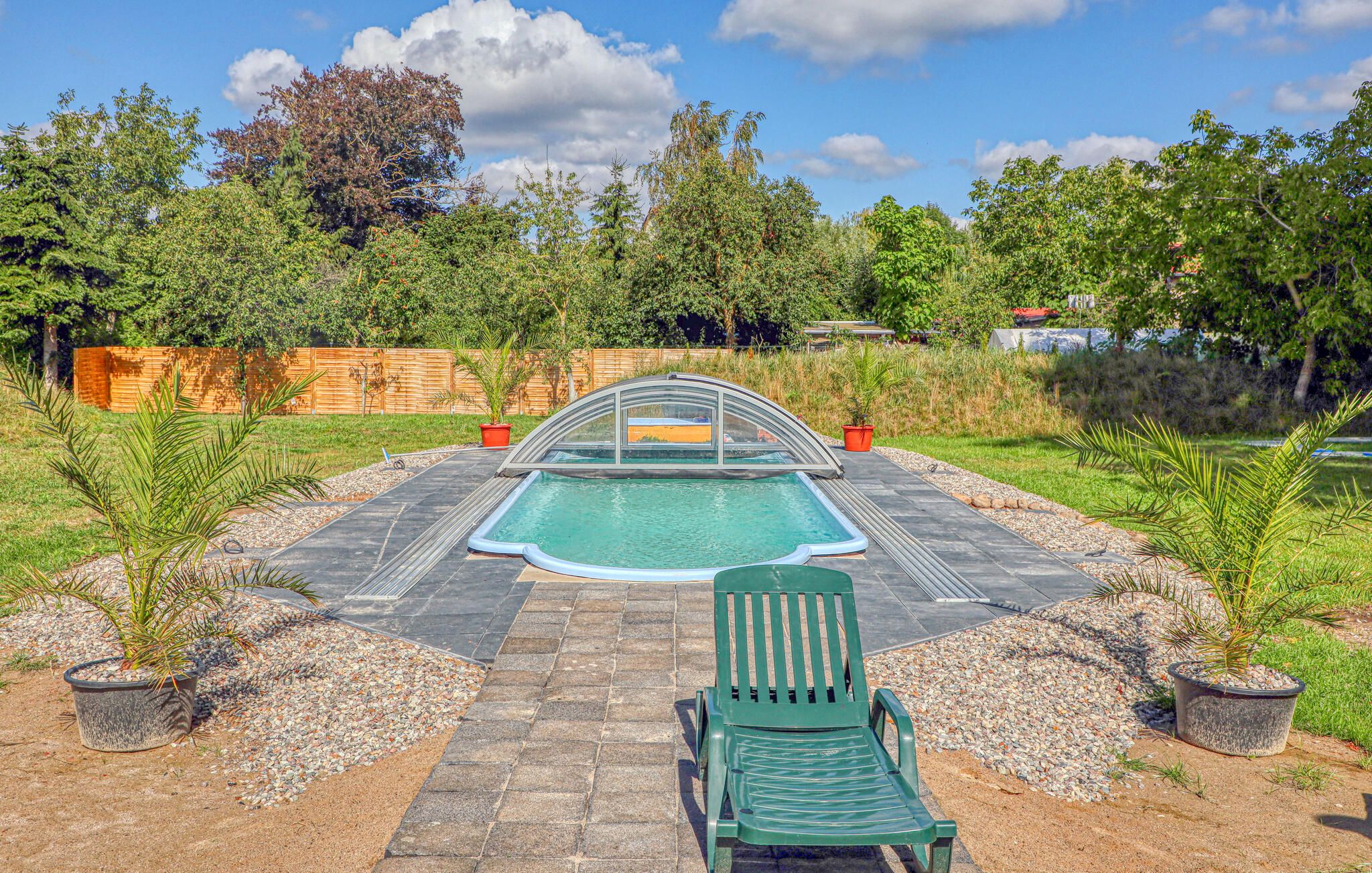 En swimmingpool med et glaslaug, omgivet af en belagt terrasse og krukker med planter.