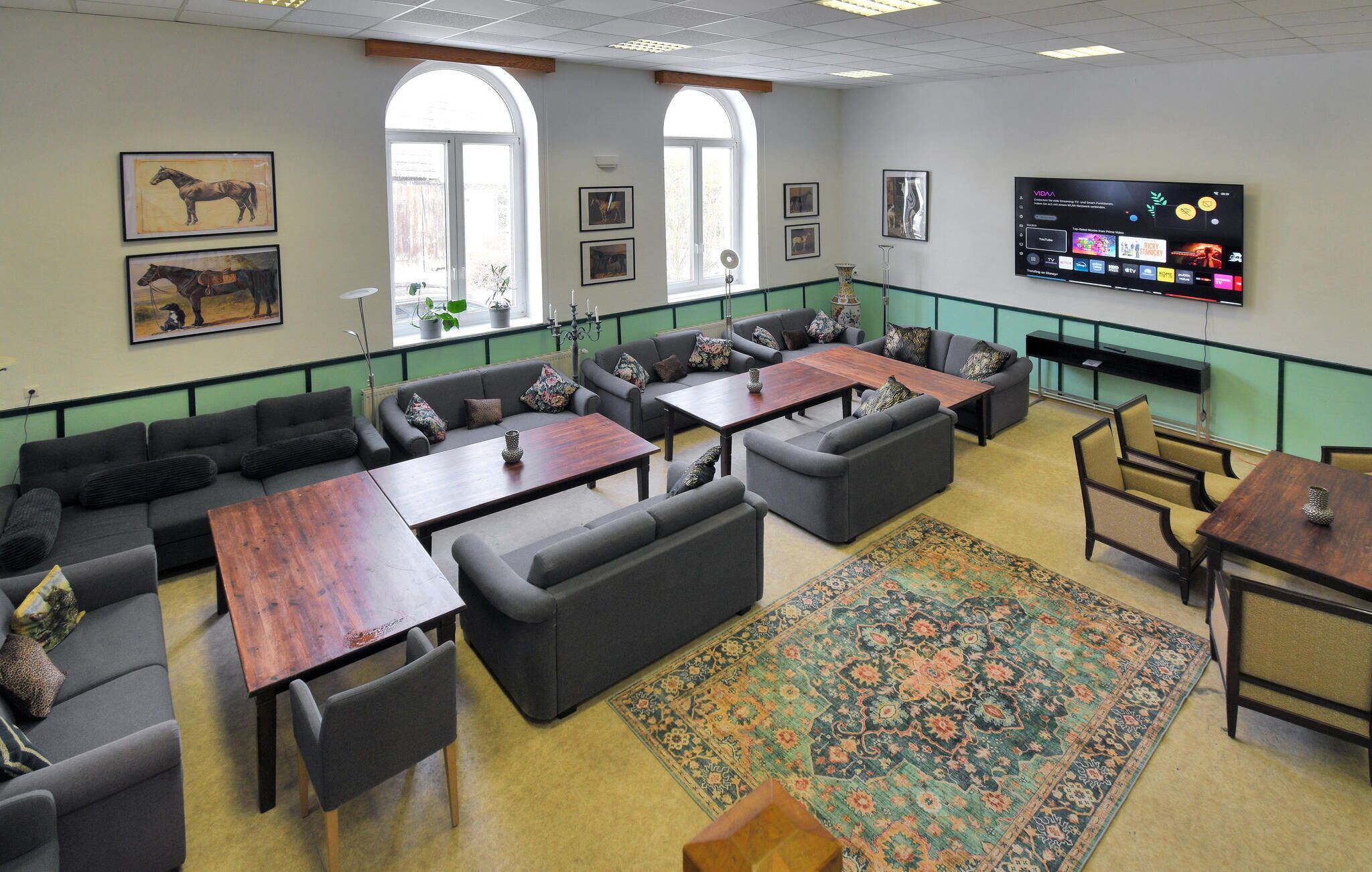 Een ruime zithoek met diverse zitplaatsen, waaronder banken en tafels, een grote flatscreen-tv en kunstwerken in lijsten aan de muren.