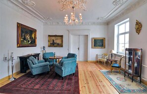 A room with a chandelier, two blue armchairs, a wooden floor, and a large window. - Beautiful home in Kletzin with sauna (Kletzin)