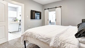 A bedroom with a large bed, a mounted TV, and a sliding door leading to a bathroom. - The Yellow Door – Cozy Indianapolis Retreat (Indianapolis)