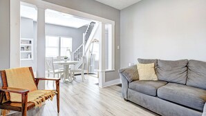 A living room with a grey sofa, wooden armchair, and a staircase leading to an upper floor. - The Yellow Door – Cozy Indianapolis Retreat (Indianapolis)