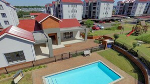 A residential building with a swimming pool, a fenced yard, and a playground.