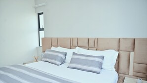 A neatly made bed with striped bedding, a headboard, and a bedside table with a vase.