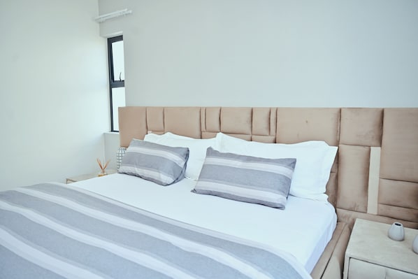 Una cama bien hecha con ropa de cama a rayas, un cabecero y una mesita de noche con un florero.