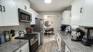 Una cocina moderna con gabinetes blancos, un refrigerador de acero inoxidable, un microondas, una estufa y una cafetera.