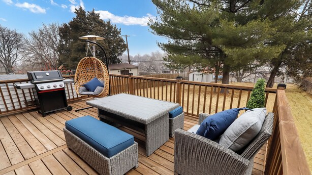 Una terraza de madera con mobiliario de mimbre, una parrilla y una silla colgante.