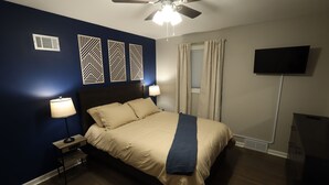 Un dormitorio con una cama, dos lámparas de noche, un ventilador de techo, un televisor y paneles decorativos en la pared.