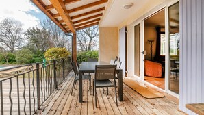 A wooden deck with a table and chairs, a glass door leading to an interior room, and a view of trees and sky. - Villa La Bulle - Piscine Privée (Grambois)