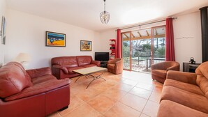 A living room with a red leather sofa, a TV, and a table. There are two paintings on the wall and a window with red curtains. - Villa La Bulle - Piscine Privée (Grambois)
