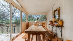 A dining area with a wooden table, benches, and a large window overlooking a garden. - Villa La Bulle - Piscine Privée (Grambois)