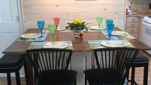 Een eetgedeelte met een houten tafel, zwarte stoelen en kleurrijk glaswerk.