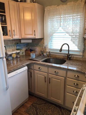 A kitchen with a granite countertop, stainless steel sink, and white cabinetry. - Perfect 2-bedroom plus sleeping porch house with AC in peaceful sleeps 6 (Lavallette)
